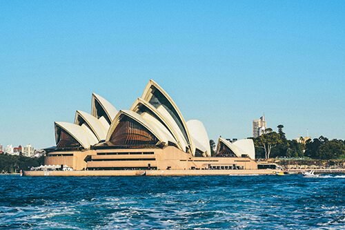 he Sydney Opera House with a clear blue sky and ocean waves, representing Australia as a key destination for student visa applicants. 